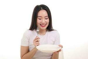 schön jung Süd Osten asiatisch Frau so tun als ob Schauspielkunst posieren halten leeren Gabel Löffel Weiß Teller im Hand Essen Geschmack aussehen sehen Weiß Hintergrund Lächeln glücklich foto