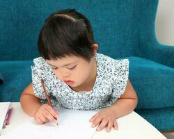 Süd-Ost asiatisch klein wenig Mädchen Kind spielen Zeichnung Gekritzel Stift Papier sie haben runter Syndrom foto