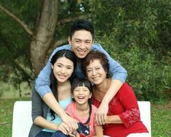 Süd-Ost asiatisch Mehrgenerationen Familie Eltern Tochter Oma Vater Mutter Kind Pose glücklich sitzen Stand draussen Park foto