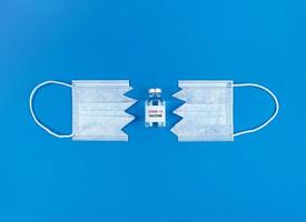 Fläschchen mit covid19-Impfstoff zwischen zwei Teilen der geschnittenen medizinischen Maske auf blauem Grund foto