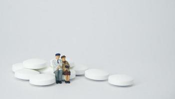 ältere Ehepaarfiguren, die auf einem Stapel weißer Pillen sitzen foto