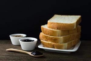geröstete Brotscheiben auf einem einzigen weißen Teller auf Holztisch mit schwarzem Hintergrund und schwarzer Johannisbeermarmelade in der kleinen Tasse und auf dem Holzlöffel foto
