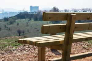 Leere Holzbank im Frühlingspark über der Stadt schließen