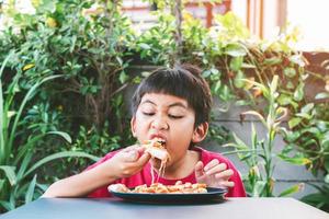 asiatischer süßer Junge, der glücklich sitzt und Pizza isst