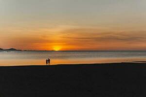 Silhouette von Familie suchen Sonnenuntergang auf das Strand. foto