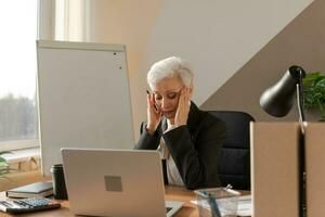 Senior Frau berühren Tempel erleben Stress im Büro. reifen Dame müde von Arbeiten Gefühl Kopfschmerzen krank Reiben Tempel Stirn. lange Laptop Verwendungszweck Computer Vision Syndrom. Büro Syndrom. foto