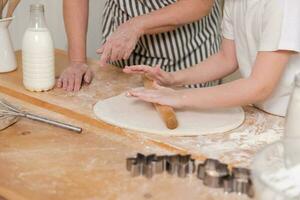 glücklich Familie im Küche. Oma Enkelin Kind Hände rollen aus Teig auf Küche Tabelle zusammen. Oma Lehren Kind Mädchen Koch backen Kekse. Haushalt Zusammenarbeit Portion Familie Generationen. foto