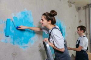 Paar im Neu Zuhause während Reparatur funktioniert Gemälde Mauer zusammen. glücklich Familie halten Farbe Walze Gemälde Mauer mit Blau Farbe Farbe im Neu Haus. Zuhause Renovierung DIY erneuern Zuhause Konzept. foto