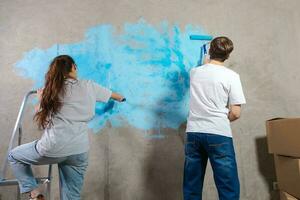 Paar im Neu Zuhause während Reparatur funktioniert Gemälde Mauer zusammen. glücklich Familie halten Farbe Walze Gemälde Mauer mit Blau Farbe Farbe im Neu Haus. Zuhause Renovierung DIY erneuern Zuhause Konzept. foto