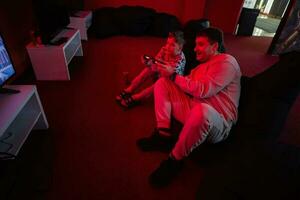 Vater und Sohn abspielen Gamepad Video Spiel Konsole im rot Spielen Zimmer. Papa und Kind Spieler. foto