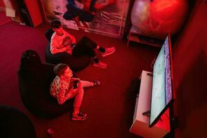 zwei Jungs Spieler abspielen Fußball Gamepad Video Spiel Konsole im rot Spielen Zimmer. foto