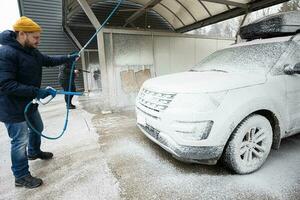 Mann wäscht amerikanisches SUV-Auto mit Dachträger in einer Selbstbedienungswäsche bei kaltem Wetter. foto