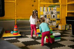 zwei Schwestern spielen beim Kinder abspielen Center während bauen mit farbig Plastik Blöcke. foto