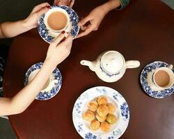 oben Aussicht von Tee trinken Party Frau Hände Gießen Teilen Teekanne Teetasse Untertasse traditionell Keks asiatisch Kleid foto