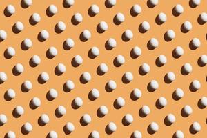 minimales Muster aus weißen Eiern unter hellem Licht mit dunklen Schatten auf orangefarbenem Hintergrund foto