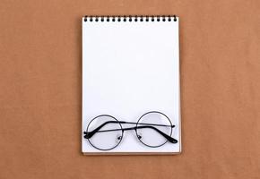 flaches Draufsichtfoto der Brille und des Notizblocks auf einem beigen abstrakten Hintergrund mit minimalem Stil des Kopierraums foto