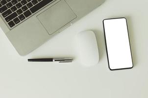 Laptop, Maus, Stift und ausgeschnittener Smartphone-Bildschirm auf einem weißen Schreibtisch foto