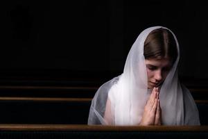 Ein junges bescheidenes Mädchen mit einem Taschentuch auf dem Kopf sitzt in der Kirche und betet foto