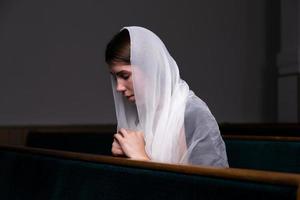 Ein christliches Mädchen im weißen Hemd betet mit demütigem Herzen in der Kirche foto