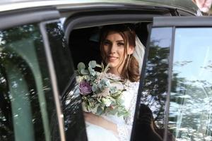 Hochzeitsfoto der Braut, die im Auto mit einem Blumenstrauß sitzt