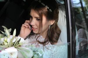 Hochzeitsfoto der Braut, die im Auto mit einem Blumenstrauß sitzt und am Telefon spricht