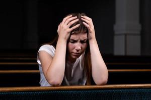 Ein trauriges christliches Mädchen im weißen Hemd sitzt und betet mit demütigem Herzen in der Kirche foto