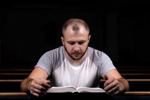 Ein junger Mann sitzt auf einer Kirchenbank, liest die Bibel und betet