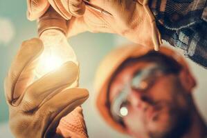 glühend Licht Birne im das Hände von ein Elektriker foto