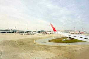 Bangkok, Thailand 2018- draußen Aussicht von Flugzeug auf das Flughafen Runway während das Flugzeug ist Kehrtwende und bereit zu nehmen aus mit Blau Himmel und viele Luft Flugzeug und das Terminal Gebäude Hintergrund. foto