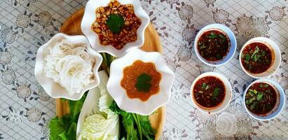 oben Aussicht von Weiß Reis Nudeln mit frisch Gemüse und Süss Soße im hölzern Tablett mit vier würzig Soße auf Tabelle zum Mittagessen beim thailändisch lokal Restaurant. Vorbereitung Essen, Diät Lebensstil und Bedienung foto