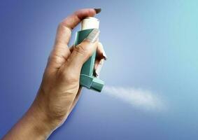 Hand halt ein Asthma Inhalator im Blau Hintergrund foto