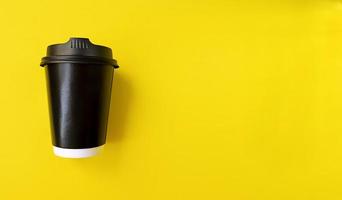 Kaffeetasse aus schwarzem Papier, um auf eine einfache Wohnung im gelben Hintergrund zu gehen, die mit minimalem Konzept des Kopierraums auf Lager liegt. Foto auf Lager