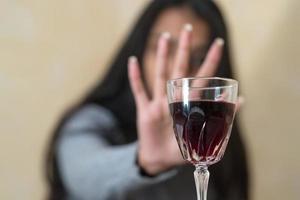 Eine junge Frau am Tisch lehnt mit ihrer Hand ein Glas Rotwein ab foto