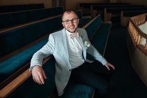 Hochzeitsfoto der Gefühle eines bärtigen Bräutigams mit Brille in einer grauen Jacke im Kirchengebäude foto