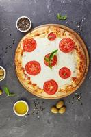 italienische Pizza und Zutaten zum Kochen auf einem schwarzen Betonhintergrund Tomatenoliven Basilikum und Gewürze