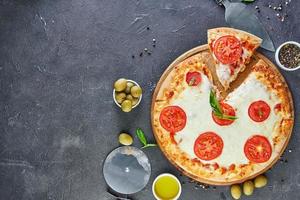 italienische Pizza und Zutaten zum Kochen auf einem schwarzen Betonhintergrund Tomatenoliven Basilikum und Gewürze