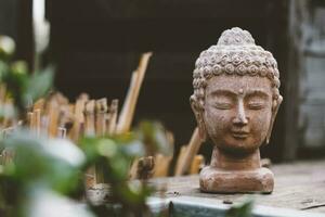 Stein Büste von Buddha auf schwarz hölzern Schreibtisch mit verschwommen Hintergrund Stehen auf das hölzern Fußboden foto