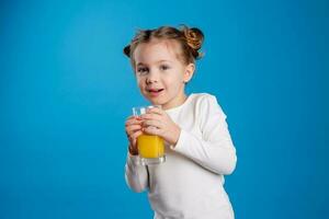 Porträt von ein wenig Mädchen von slawisch Aussehen Trinken Orange Saft auf ein Blau Hintergrund foto