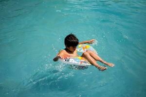 glücklich indisch Junge Schwimmen im ein Schwimmbad, Kind tragen Schwimmen Kostüm entlang mit Luft Tube während heiß Sommer- Urlaube, Kinder Junge im groß Schwimmen Schwimmbad. foto