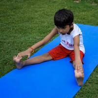 asiatisch Clever Kind tun Yoga Pose im das Gesellschaft Park draussen, Kinder- Yoga Pose. das wenig Junge tun Yoga und Meditation Übung. foto