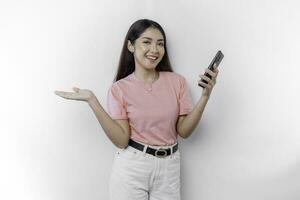 ein Porträt von ein glücklich asiatisch Frau tragen Rosa T-Shirt, halten ihr Telefon, und zeigen Kopieren Raum auf neben ihr, isoliert durch Weiß Hintergrund foto