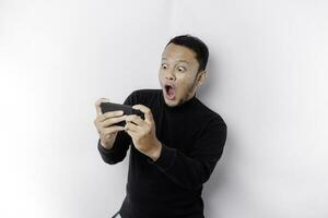 jung asiatisch Mann im beiläufig tragen ist spielen Spiele mit Handy, Mobiltelefon Telefon mit ein Weiß Hintergrund isoliert. foto