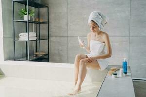 Frau massiert Bein mit natürlicher Anticellulite-Hautpflegekosmetik im Badezimmer. körperpflege behandlung foto