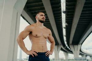 sportlich männlich Fitness Modell- posiert mit muskulös Körper, konzentriert draussen. regulär Sport Übungen zum ein aktiv Lebensstil. foto
