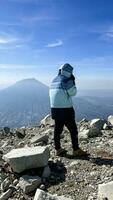 asiatisch Mann Stehen auf oben von ein in der Nähe Berg suchen beim montieren sindoro. Westen Java, Indonesien, März 16, 2023 foto