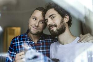 jung Fröhlich Paar im Liebe suchen aus das Fenster. zwei jung androgyn Männer lächelnd zusammen und haben Kaffee. foto