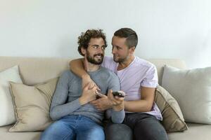jung homosexuell Paar entspannend auf Sofa im das Leben Zimmer, Umarmen und genießen während Aufpassen Fernseher foto