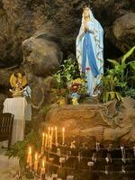 Statue von heilig Jungfrau Maria im römisch katholisch Kirche, im das Höhle von Jungfrau Maria, im ein Felsen Höhle Kapelle katholisch Kirche mit tropisch Blumen um foto