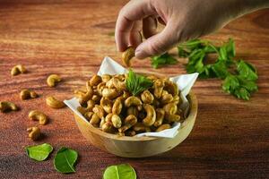 Cashew Mutter, im Indonesien bekannt wie kacang Mete oder Mede, serviert im ein Schüssel auf Holz Hintergrund, mit Hand foto