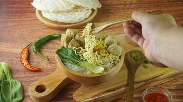 Frikadelle, im Indonesien bekannt wie Bakso oder Baso. serviert mit Nudeln Gemüse Chili Soße im ein Schüssel auf Holz Hintergrund mit Hand. schließen oben oben Aussicht eben legen Kopieren Raum foto